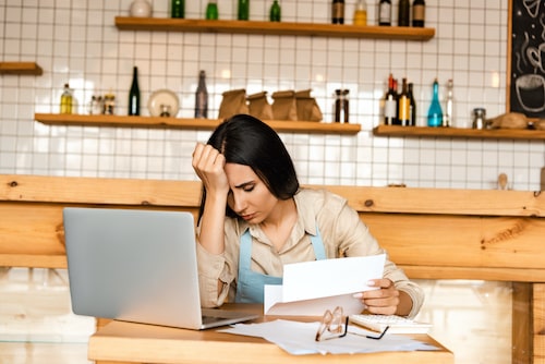 Lady-sitting-at-table-in-kitchen-reading-paper-with-hand-on-forehead