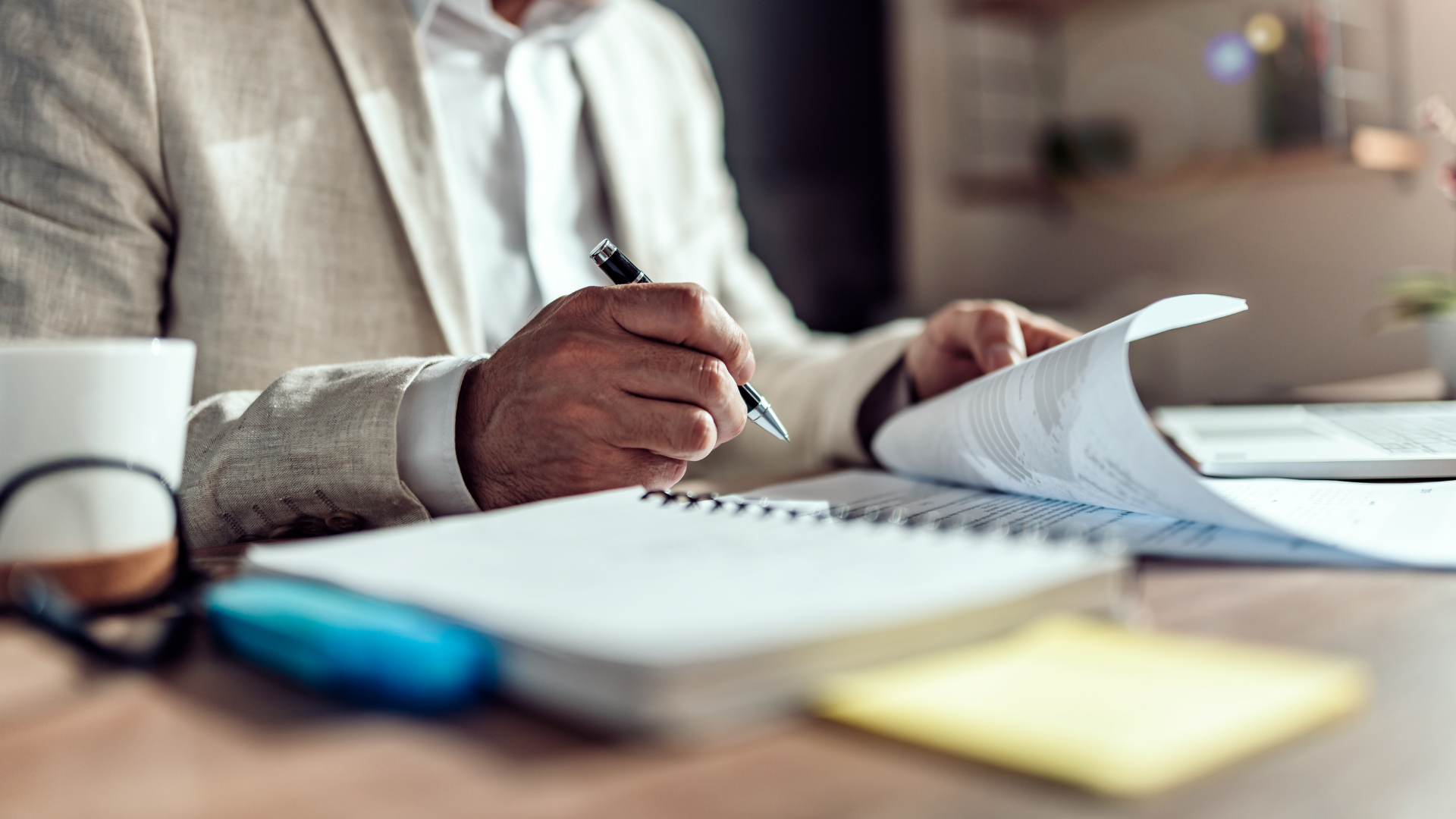 Male-in-suit-writing-with-pen-in-notebook-at-desk