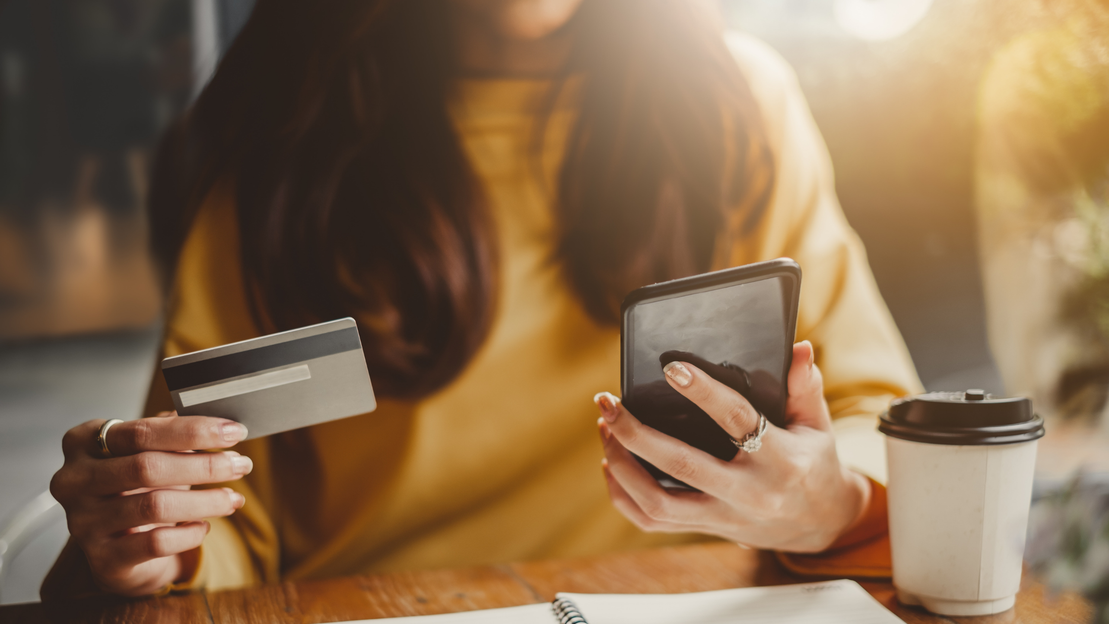 woman in yellow top holding credit card in one hand and cellphone in the other hand